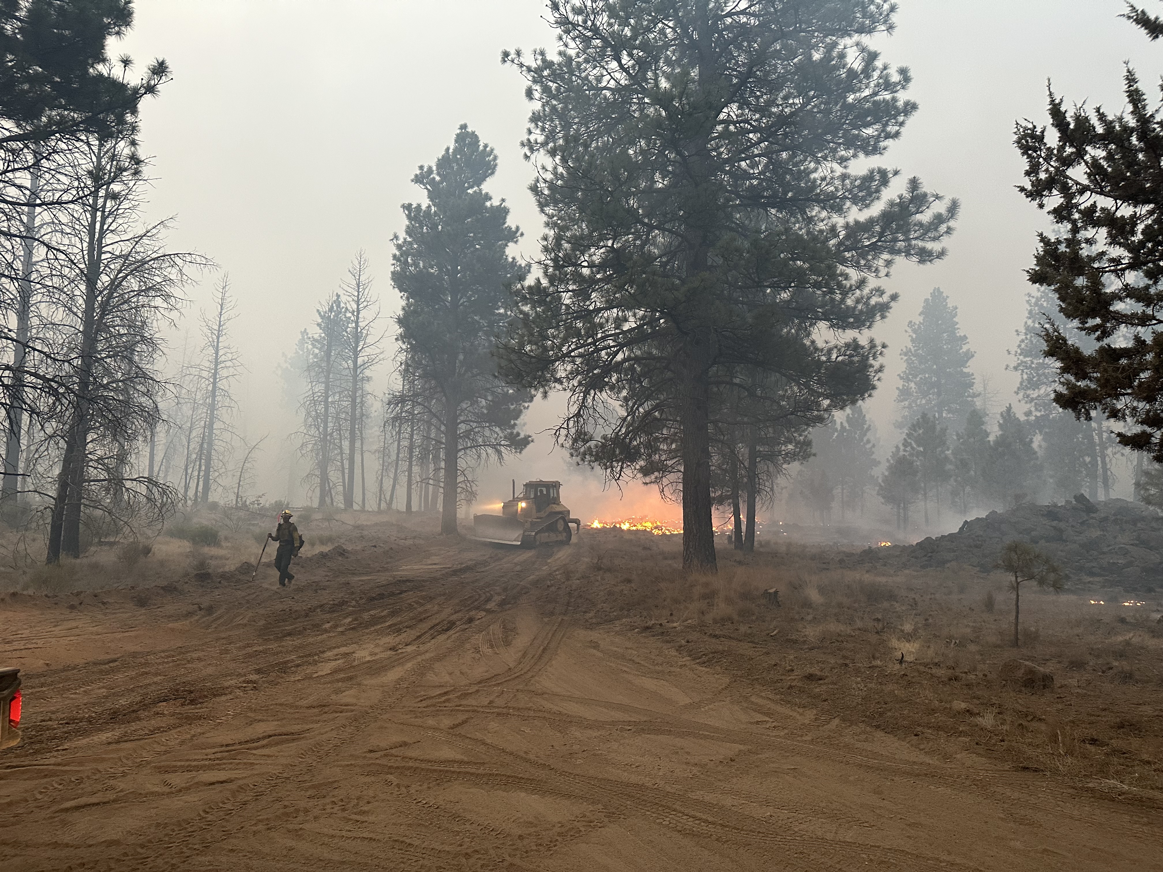 Dozer and firefighter fighting a large fire.