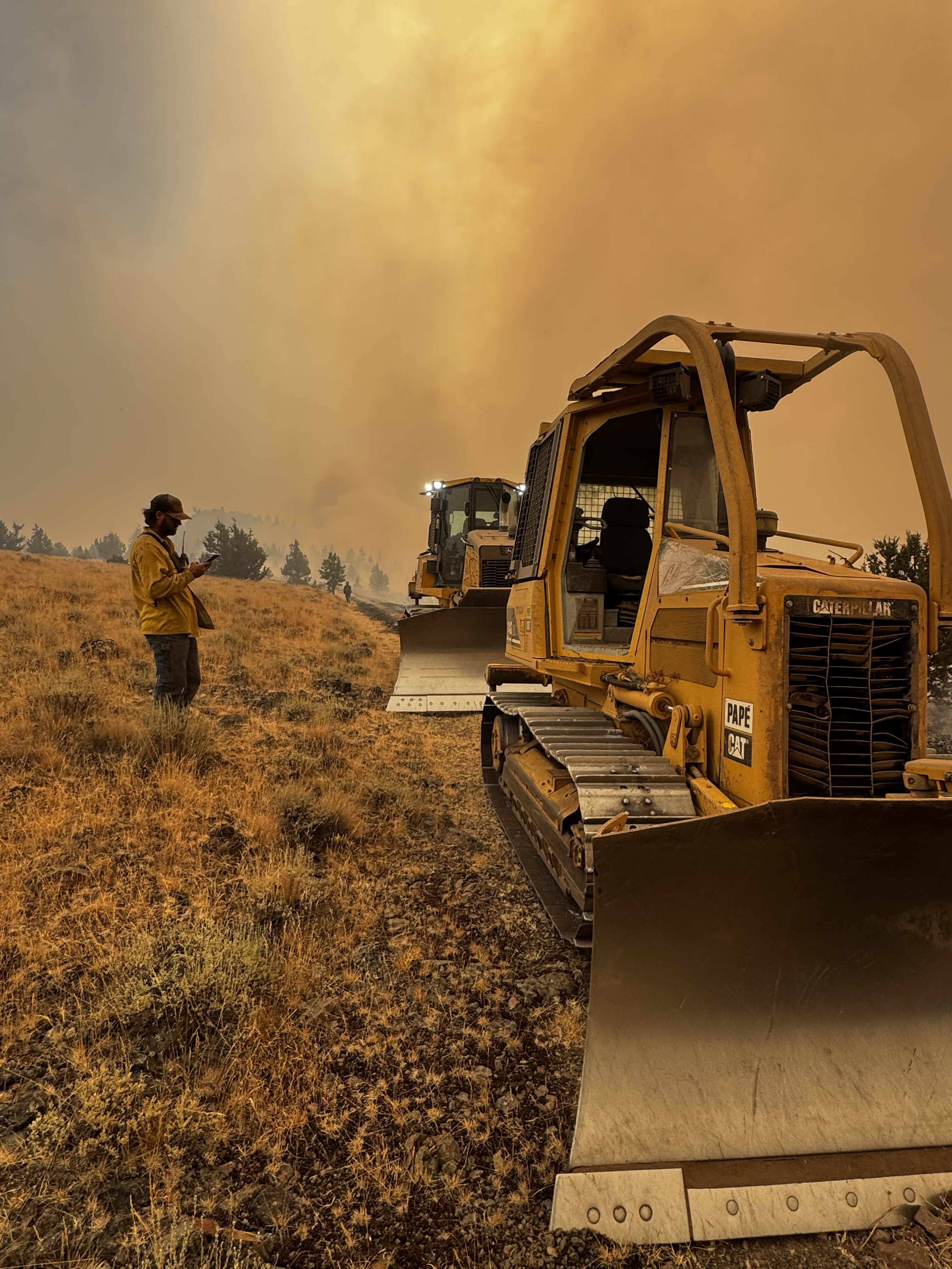 brewer-crosswhite-dozer-and-smoke Two dozers and a firefighter in a smoked filled field.